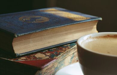 Två äldre böcker med rikt dekorerade pärmar bredvid en kopp kaffe